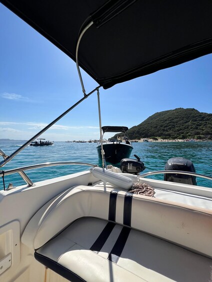 A boat with a black canopy, a white interior, and a view of the sea with other boats and a green hill in the background. 1