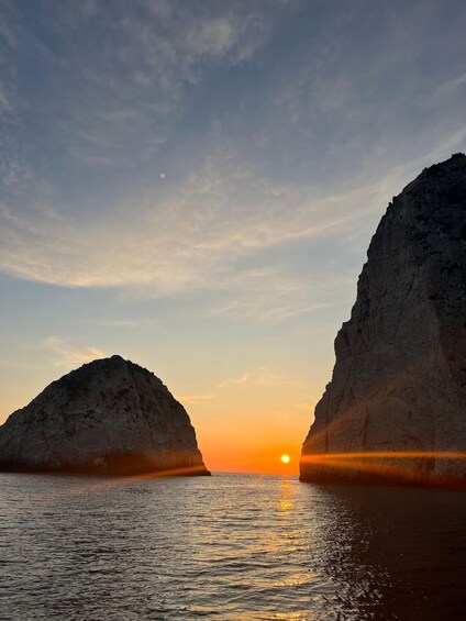 A sunset over a body of water with two prominent rock formations on either side. 3
