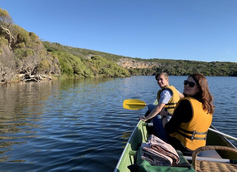 Two people in a green canoe on a calm lake surrounded by greenery. 1