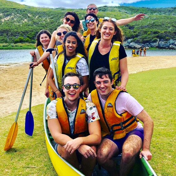A group of people in a yellow canoe on a grassy area near a body of water with hills in the background. 5