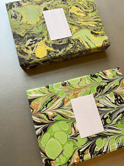 Deux boîtes à motifs marbrés, portant des étiquettes, sont posées sur une table. 2