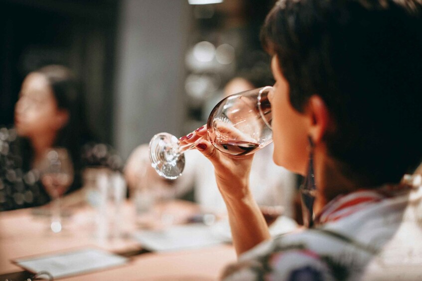 A person holding a wine glass, seated at a table with other diners in a dimly lit restaurant. 5