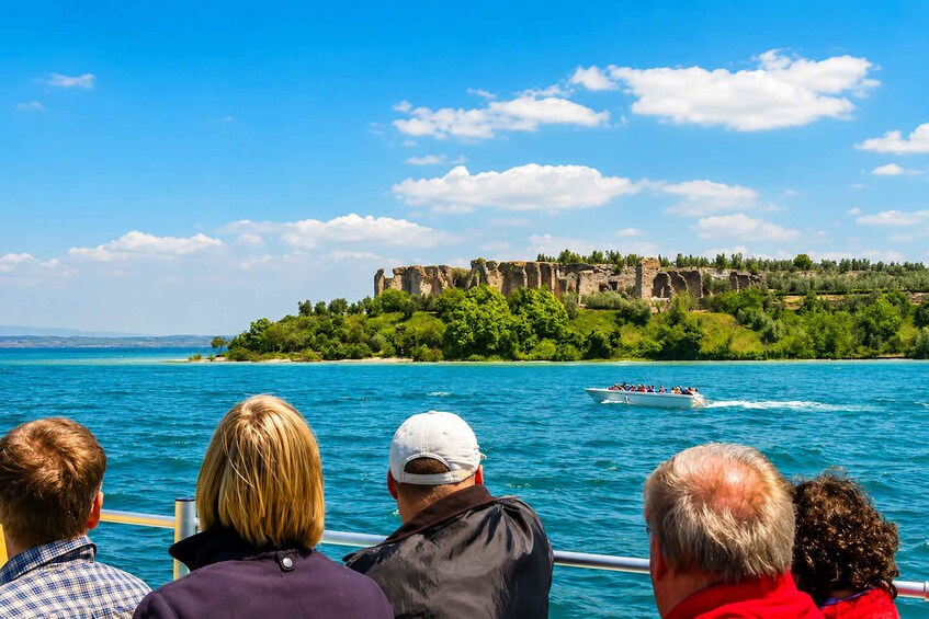 Un grupo de personas en un bote, una isla rocosa con ruinas y un cielo azul despejado. 5