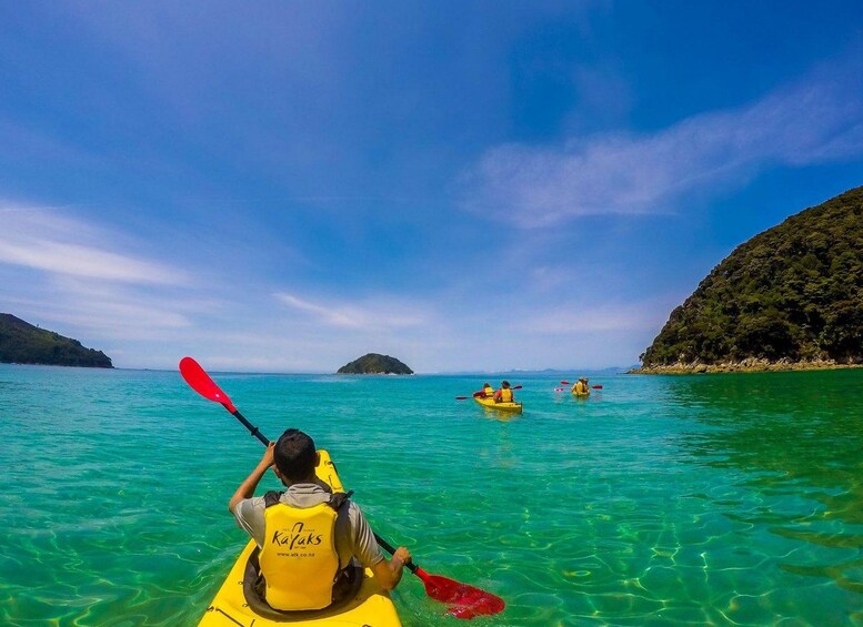 Una persona haciendo kayak en aguas turquesas cristalinas, con un paisaje montañoso al fondo. 4