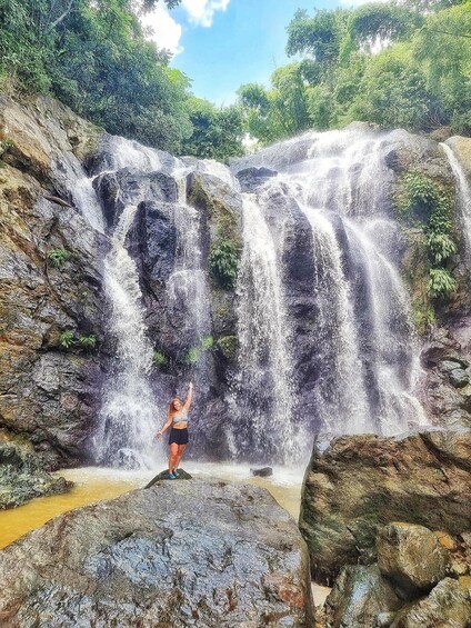 Una cascada con una persona de pie sobre una roca al frente. 1