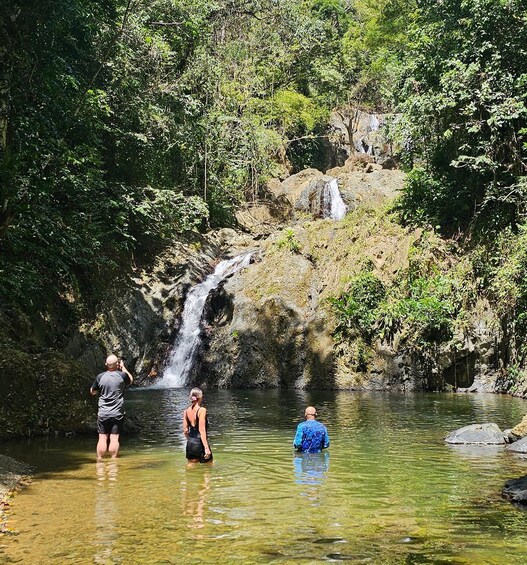 Una cascada en un área boscosa con gente de pie en el agua. 5