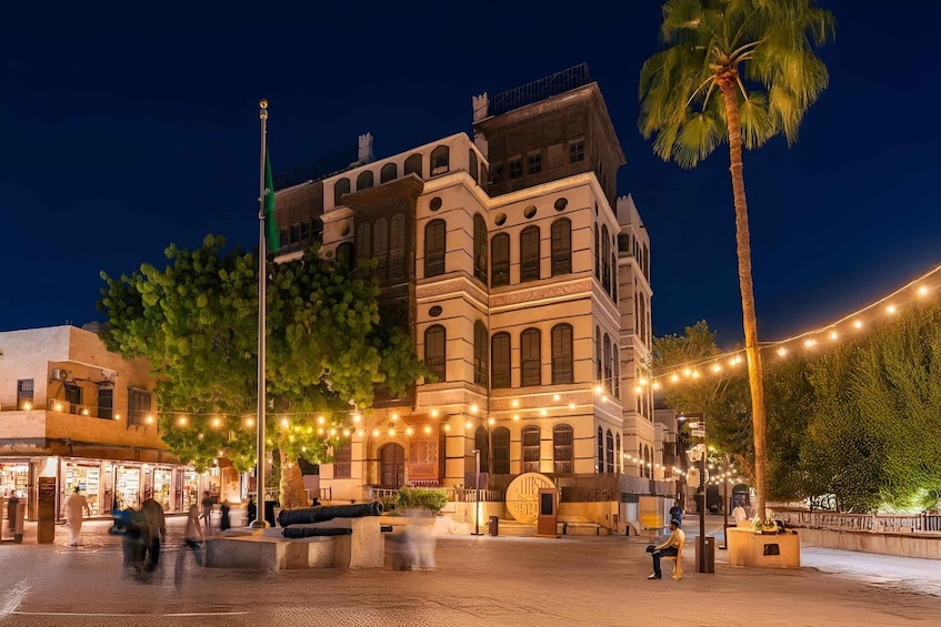 Un edificio histórico con ventanas de arco y un balcón, rodeado de palmeras y luces colgantes. 4