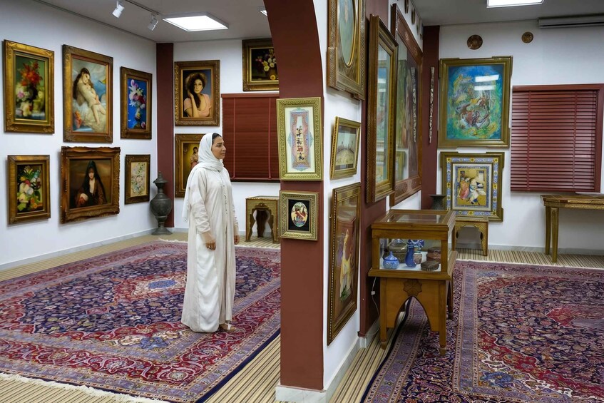 Una habitación con una amplia colección de obras de arte enmarcadas en las paredes, un suelo con alfombra estampada y una persona vestida con traje tradicional. 5
