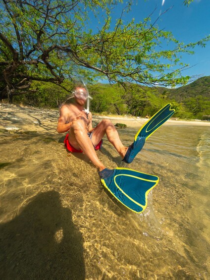 A person snorkeling in clear shallow water with a forested background. 2