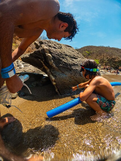 A person playing with a blue toy in shallow water near a large rock. 3