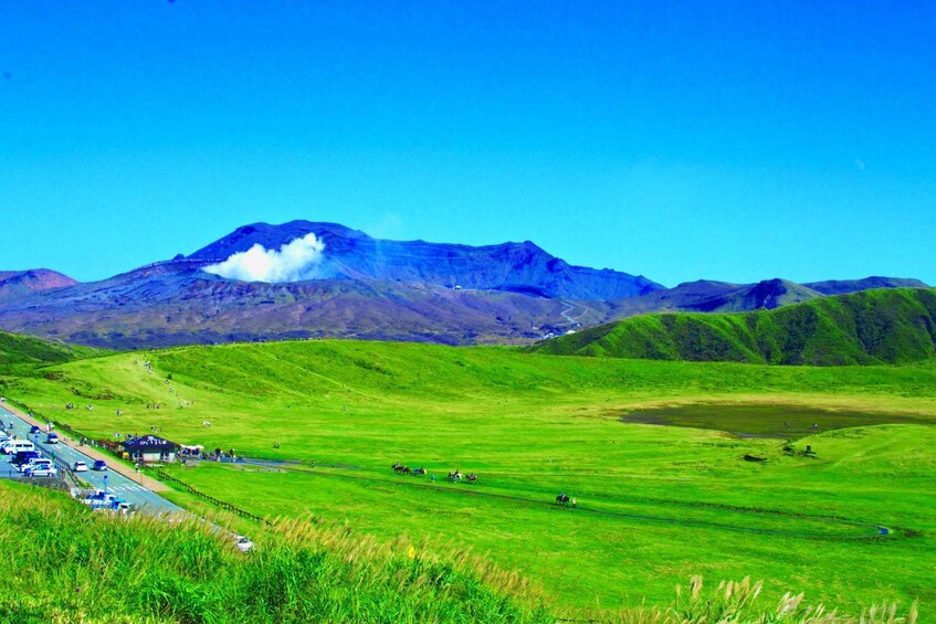 A mountainous landscape with a clear sky, green fields, and a road with vehicles. 3