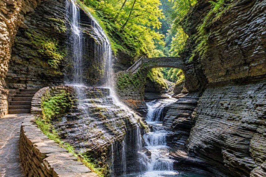 A waterfall cascading over a stone bridge surrounded by lush greenery. 3
