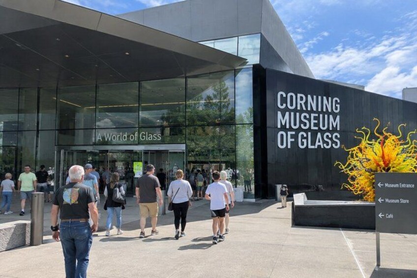 The Corning Museum of Glass entrance with people walking in front. 2