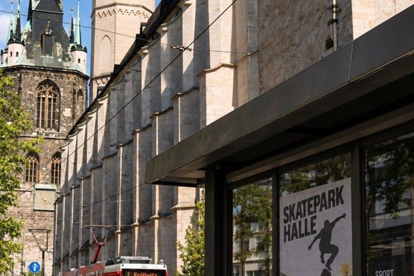 A building with a sign for Skatepark Halle and a historic church in the background. 2
