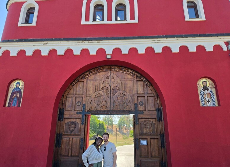 A red building with a large wooden gate, two small windows with religious icons, and a couple standing in front. 5