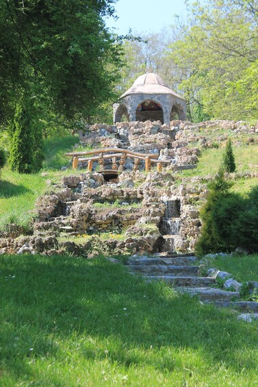 A stone structure with a dome and arches, surrounded by greenery and a small waterfall. 4