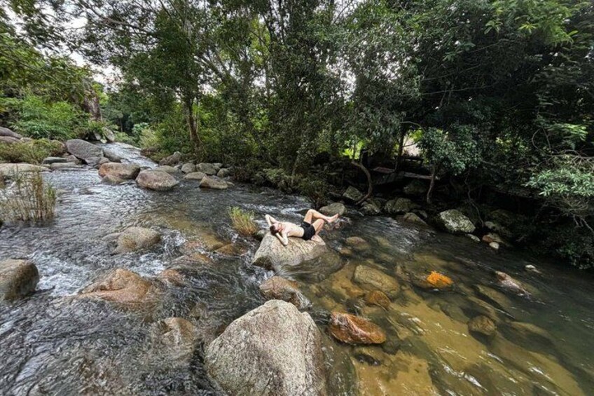 A person relaxing on rocks by a flowing river surrounded by dense greenery. 5