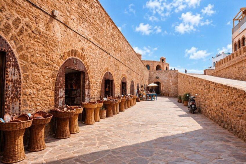 A stone building with arched doorways, a paved walkway, and wicker baskets. 5