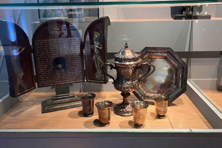 A display case with a brass teapot, cups, and a decorative plaque. 3