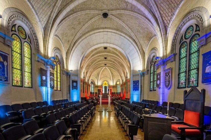 A church interior with arched ceilings, stained glass windows, rows of pews, and a central aisle leading to the altar. 1
