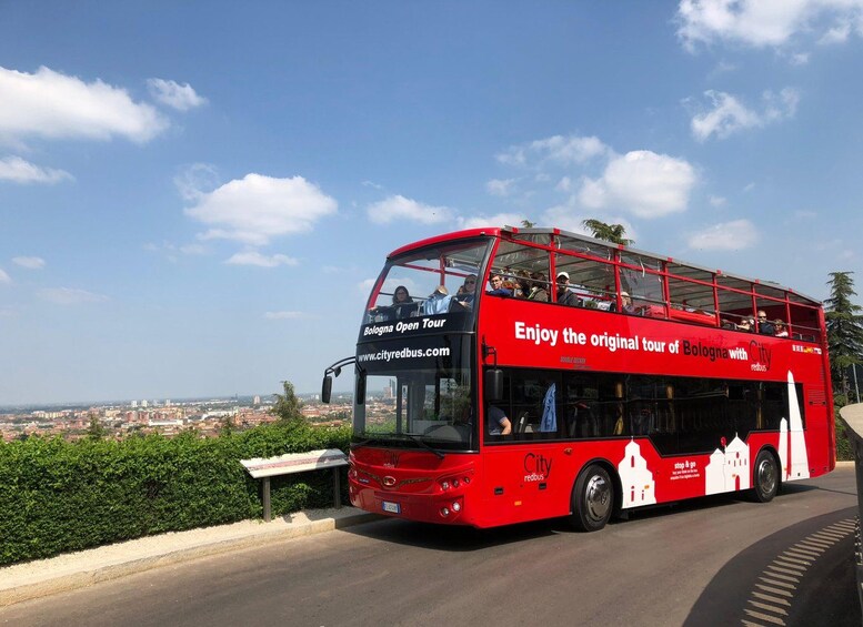 Punainen kaksikerroksinen bussi, jonka kyljissä on mainoksia, joissa mainostetaan «Bologna Open Tour» -kiertoajelua ja «Nauti Bolognan alkuperäisestä kiertoajelusta City redbus -bussilla». 1