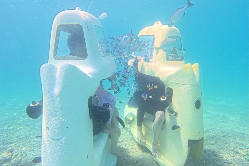 Two underwater vehicles with people inside, surrounded by fish. 4