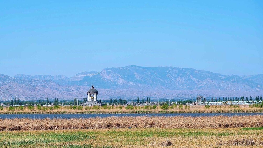 A landscape with a large mountain range in the background, a body of water in the foreground, and a structure with a dome in the middle ground. 2