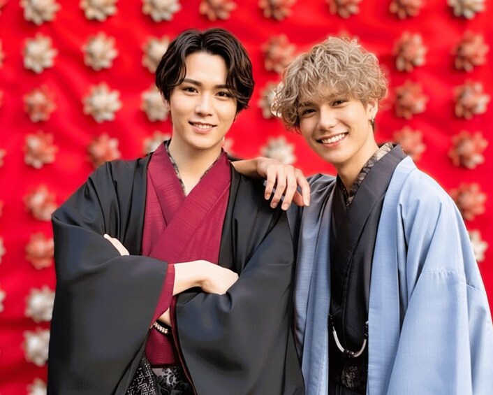 Two individuals in traditional attire against a red floral background. 3