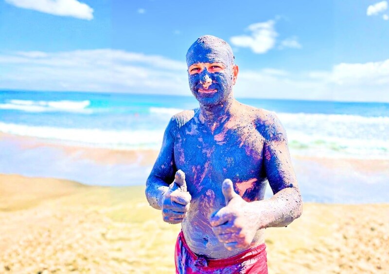 Una persona cubierta de polvo azul en una playa, con olas al fondo. 3