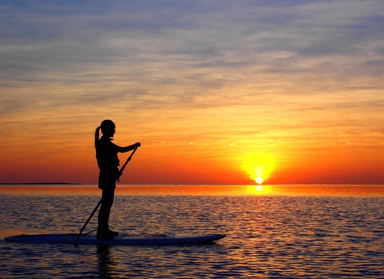 Una persona fa paddleboarding al tramonto, con il sole che scompare all'orizzonte. 1
