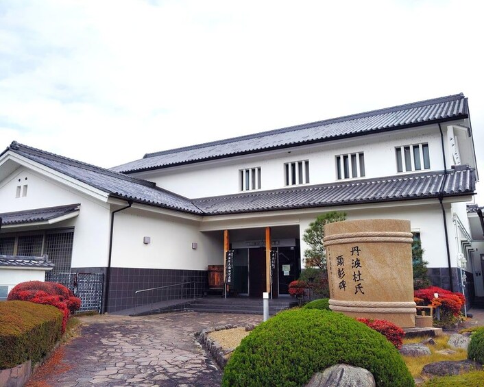 A traditional Japanese building with a tiled roof, a stone pillar with Japanese characters, and a stone pathway leading to the entrance. 5