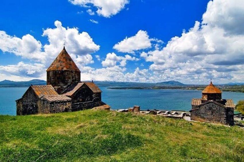 A church with a bell tower and a smaller building by a lake with mountains in the background. 1