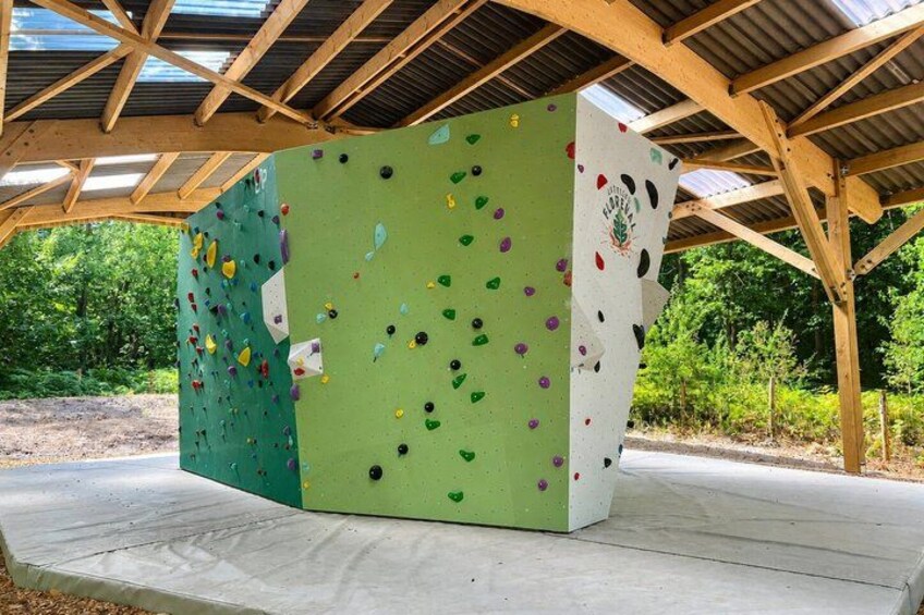 A climbing wall with various holds, set under a wooden structure with a metal roof. 3