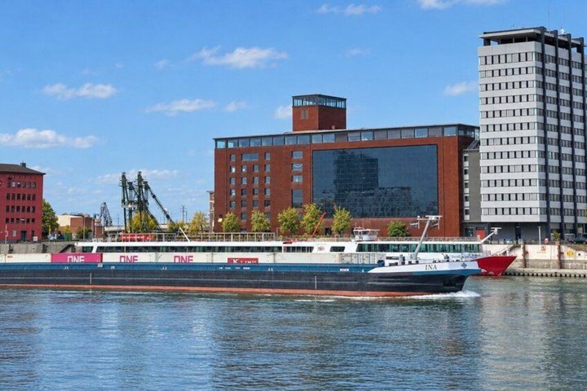 A river with a large passenger boat, buildings, and cranes in the background. 3