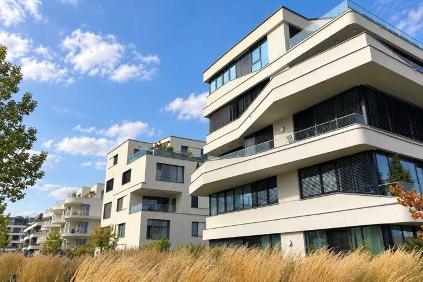A modern multi-story residential building with balconies, surrounded by tall grass and trees. 4