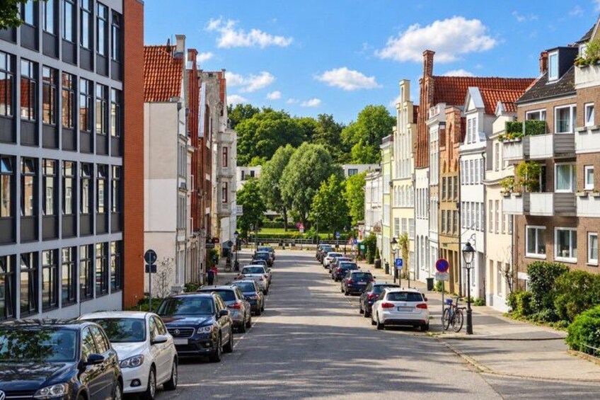 A tree-lined street with parked cars and historic buildings. 3