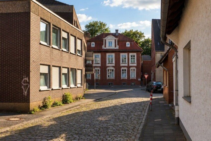 A cobblestone street, a brick building with a window, and a red brick building with a white facade. 3