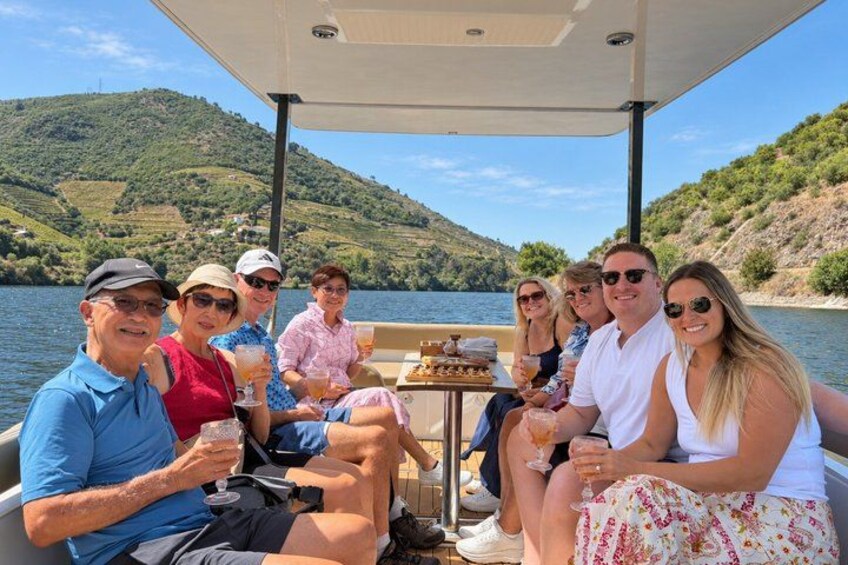 A group of people on a boat with a table, surrounded by a lake and hills. 3