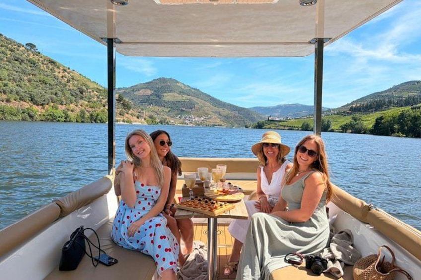 A group of people on a boat with a table of food and drinks, surrounded by a lake and hills. 1