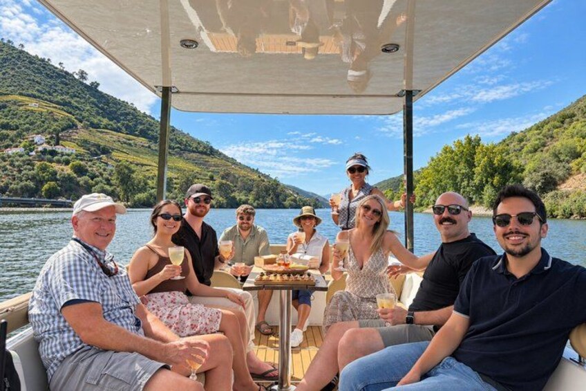 A group of people on a boat with a table of food and drinks, surrounded by a lake and hills. 5