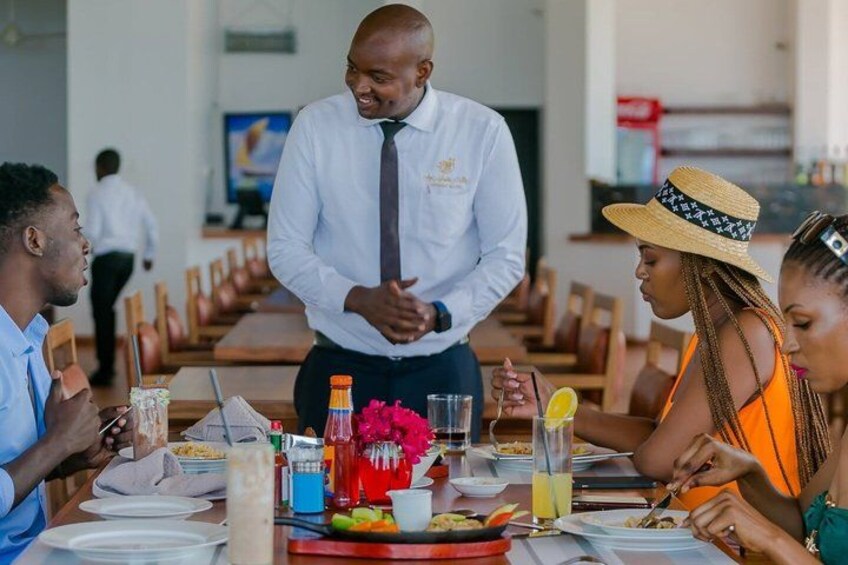 A restaurant setting with people dining, a waiter, and a table with food and drinks. 2