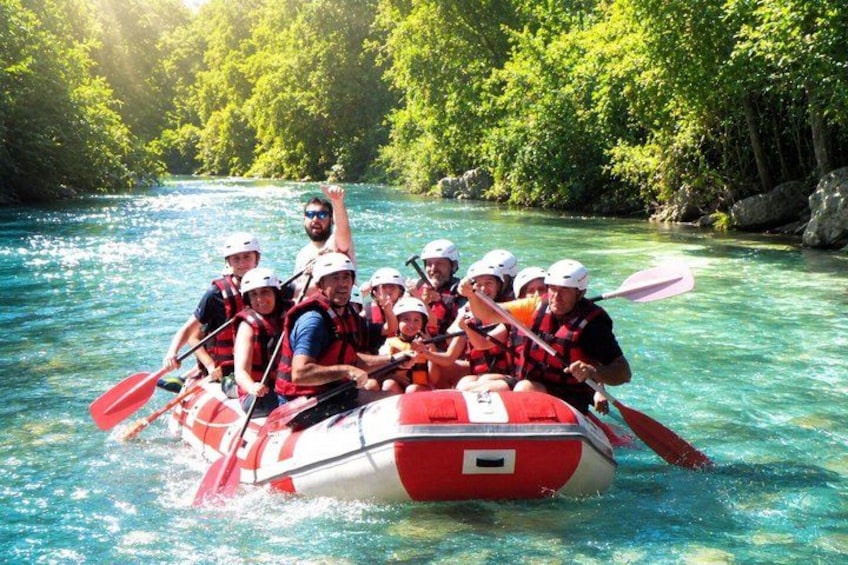 A group of people in a red and white raft on a river surrounded by lush greenery. 1