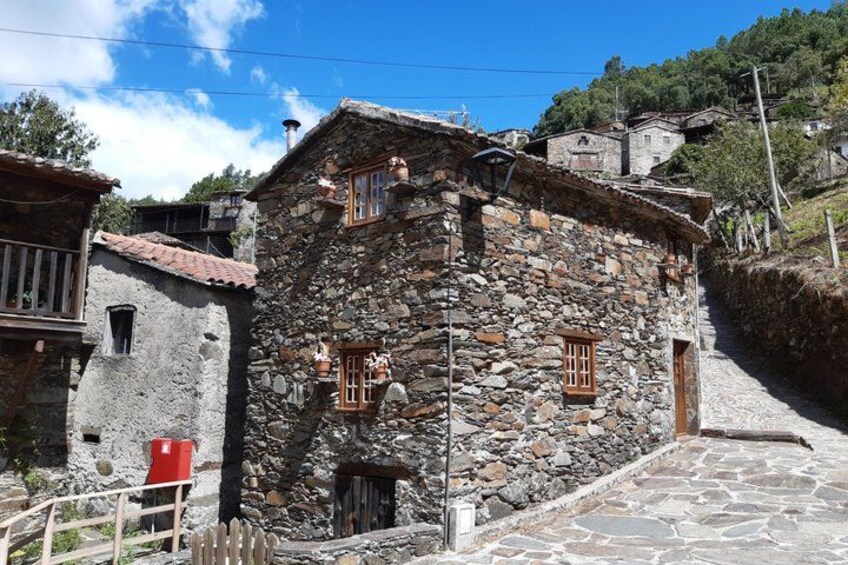 A stone building with a sloped roof, a wooden door, and a window with a grid pattern. 1