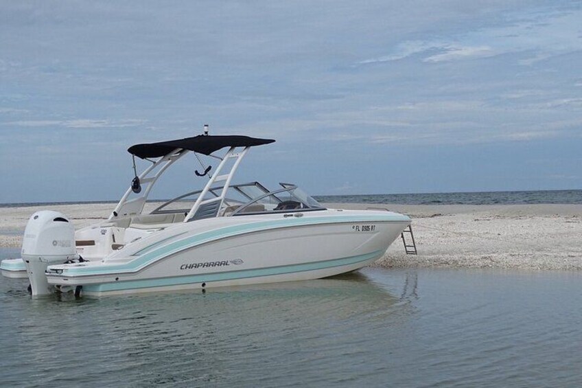 A white and light blue speedboat named 'CHAPARRAL' with a black canopy, docked on a calm beach. 1