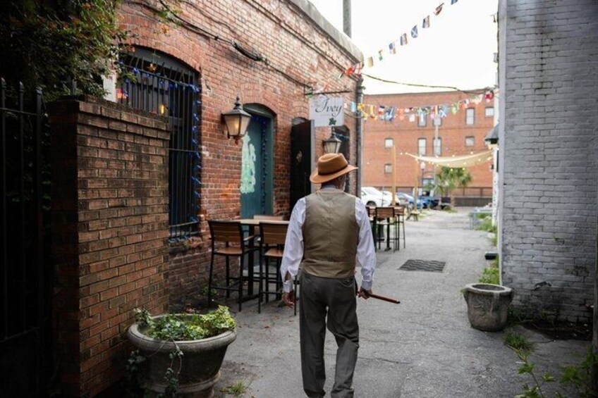 A person walking down a brick alleyway with a building on the left and a table and chairs on the right. 2