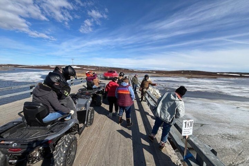 A group of people on a wooden dock by a frozen lake, some on snowmobiles. 2