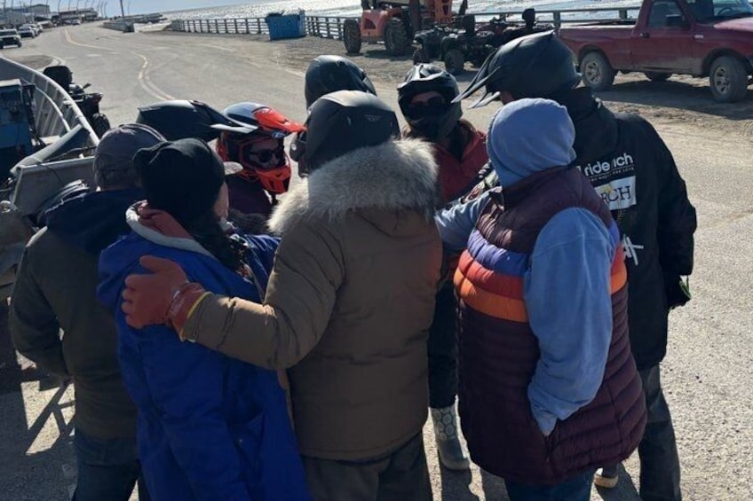 A group of people standing on a road, some wearing vests, with vehicles in the background. 4