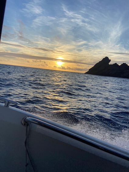 Un bote en el agua con un atardecer al fondo y un afloramiento rocoso a la derecha. 1