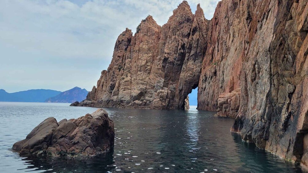 Un paisaje costero con una imponente formación rocosa que presenta un arco natural sobre el mar. 3