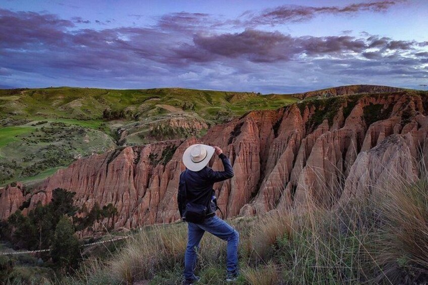 A person taking a photograph of a landscape with red rock formations and green hills. 2